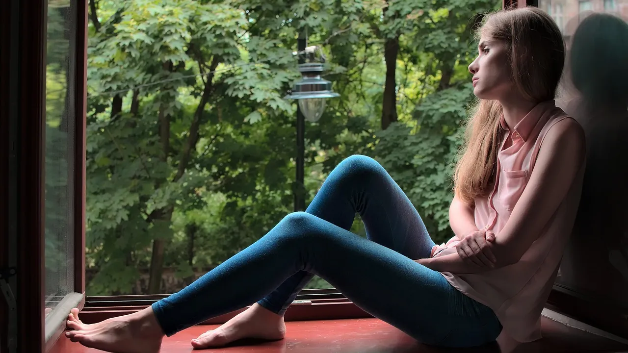 Femme assise sur le rebord d'une fenêtre ouverte, songeuse