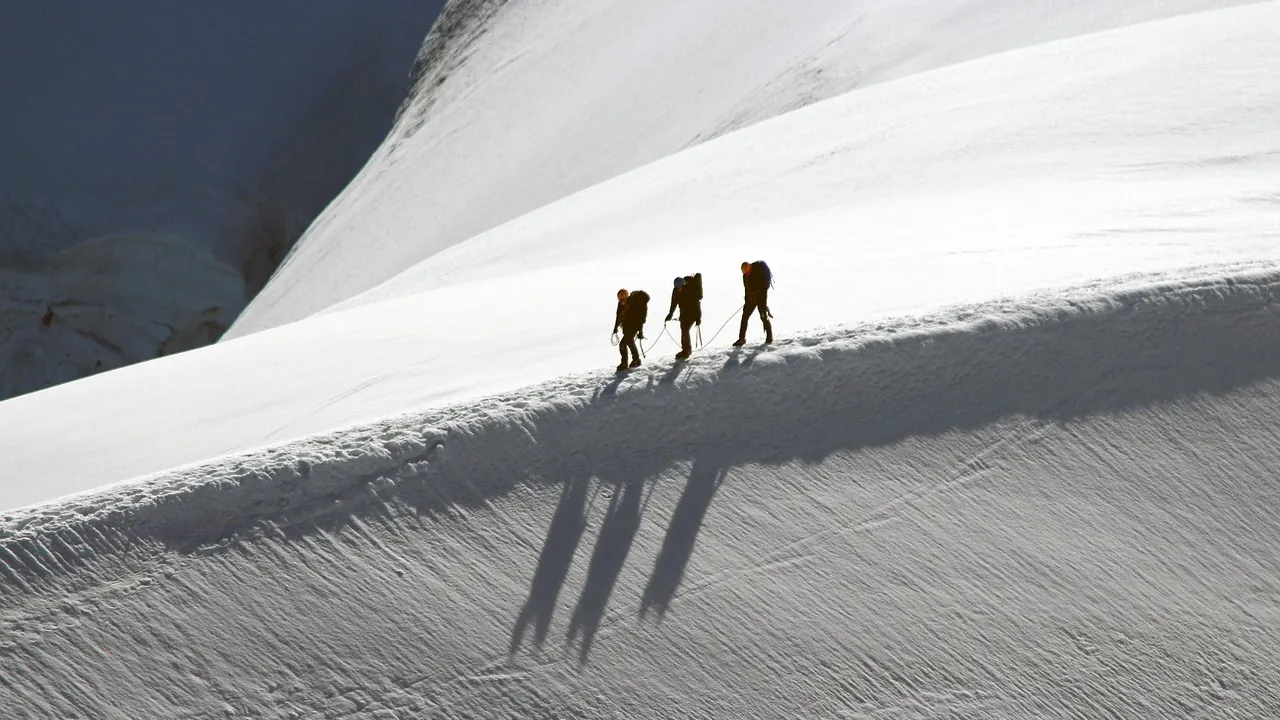 Trois alpinistes progressant en file sur une pente enneigée